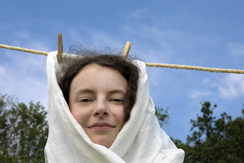 Porträt einer lächelnden jungen Frau, eingewickelt in ein weißes Tuch, das an einer Wäscheleine hängt, lizenzfreies Stockfoto
