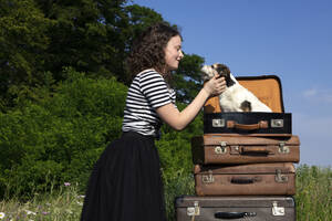 Junge Frau knuddelt kleinen Hund im Koffer sitzend - PSTF00545