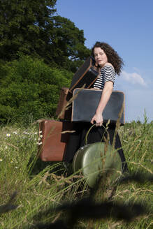 Porträt einer jungen Frau auf einer Wiese mit vielen Koffern - PSTF00552