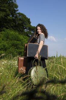 Porträt einer jungen Frau auf einer Wiese mit vielen Koffern - PSTF00553