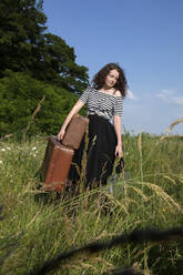 Porträt einer jungen Frau auf einer Wiese mit vielen Koffern - PSTF00554