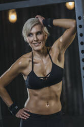 Porträt einer blonden Sportlerin mit schwarzem Sport-BH im Fitnessstudio - MADF01442