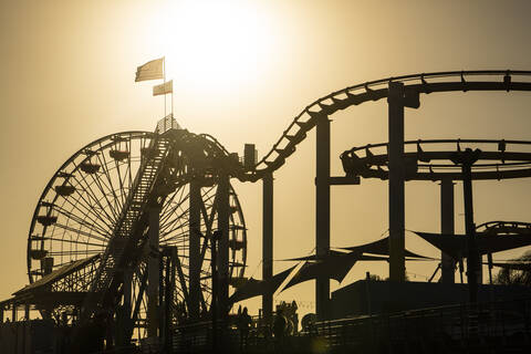 USA, Kalifornien, Santa Monica, Silhouetten von Riesenrad und Achterbahn am Santa Monica Pier bei Sonnenuntergang, lizenzfreies Stockfoto