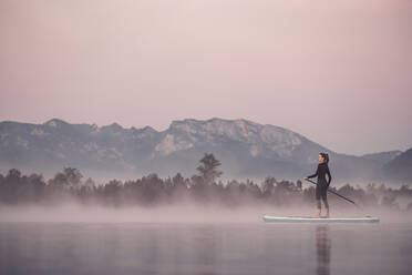 Woman stand up paddling on lake Kirchsee at morning mist, Bad Toelz, Bavaria, Germany - WFF00196