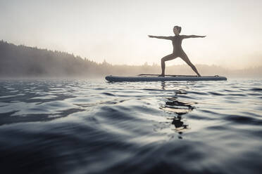 Frau beim morgendlichen Yoga mit dem Paddle Board auf dem Kirchsee, Bad Tölz, Bayern, Deutschland - WFF00198