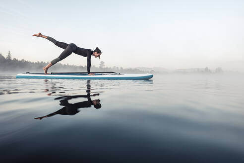 Frau beim morgendlichen Yoga mit dem Paddle Board auf dem Kirchsee, Bad Tölz, Bayern, Deutschland - WFF00199