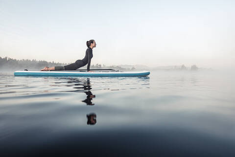 Woman practicing paddle board yoga on lake Kirchsee in the morning, Bad Toelz, Bavaria, Germany stock photo