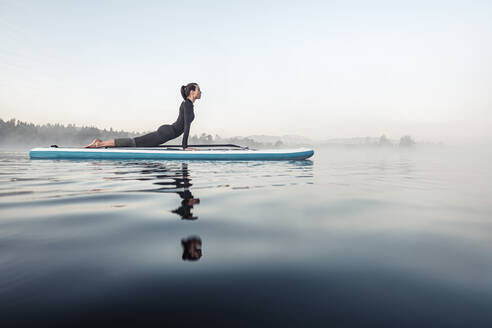 Frau beim morgendlichen Yoga mit dem Paddle Board auf dem Kirchsee, Bad Tölz, Bayern, Deutschland - WFF00200