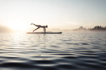 Frau beim morgendlichen Yoga mit dem Paddle Board auf dem Kirchsee, Bad Tölz, Bayern, Deutschland - WFF00201