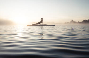 Frau beim morgendlichen Yoga mit dem Paddle Board auf dem Kirchsee, Bad Tölz, Bayern, Deutschland - WFF00202