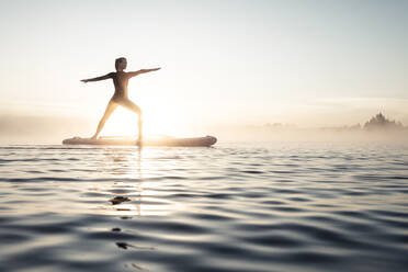 Frau beim morgendlichen Yoga mit dem Paddle Board auf dem Kirchsee, Bad Tölz, Bayern, Deutschland - WFF00204