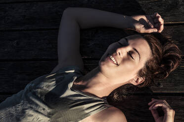 Porträt einer glücklichen Frau, die auf einem Steg im Sonnenlicht liegt - WFF00209