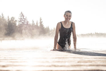 Glückliche Frau im schwarzen Badeanzug beim Baden in einem See im Morgennebel - WFF00215
