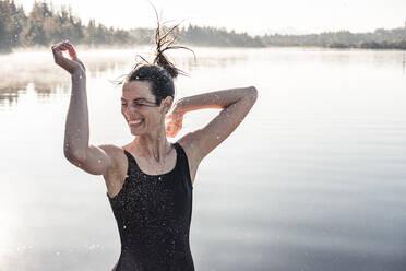 Fröhliche Frau im schwarzen Badeanzug an einem See im Morgennebel - WFF00217