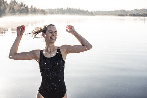 Fröhliche Frau im schwarzen Badeanzug an einem See im Morgennebel, lizenzfreies Stockfoto