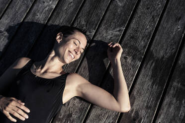 Happy woman wearing black swimsuit lying on a jetty - WFF00219