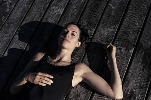 Porträt einer Frau im schwarzen Badeanzug auf einem Steg liegend, lizenzfreies Stockfoto