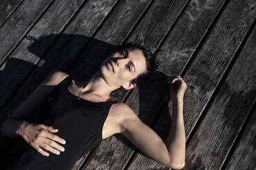Portait of woman wearing black swimsuit lying on a jetty - WFF00221