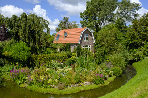 Netherlands, North Holland, Hoorn, Lake Ijssel ditch stretching in front of blooming garden of rustic house stock photo