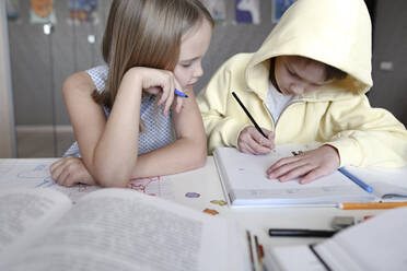 Brother and sister sitting at table at home doing homework together - EYAF00741