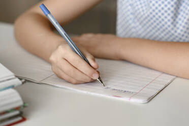 Nahaufnahme eines Mädchens, das zu Hause am Tisch sitzt und in ein Arbeitsbuch schreibt - EYAF00744