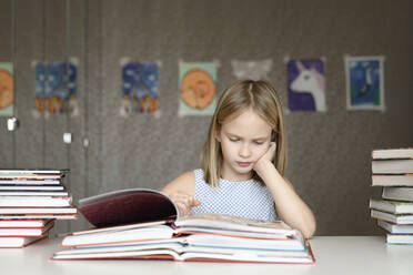 Girl sitting at table at home reading books - EYAF00745