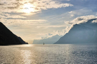 Italien, Trentino, Nago-Torbole, Silhouette eines Segelboots in der Nähe der Küstenklippen des Gardasees bei stimmungsvollem Sonnenaufgang - MRF02306