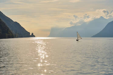 Italy, Trentino, Nago-Torbole, Silhouette of sailboat sailing near coastal cliffs of Lake Garda at moody dawn - MRF02307