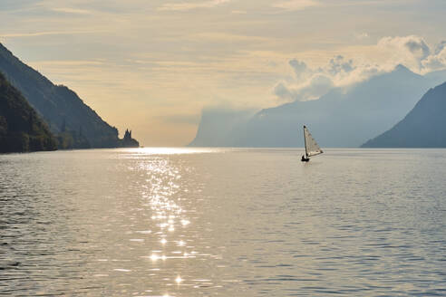 Italien, Trentino, Nago-Torbole, Silhouette eines Segelboots in der Nähe der Küstenklippen des Gardasees bei stimmungsvoller Morgendämmerung - MRF02307