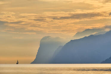 Italien, Trentino, Nago-Torbole, Silhouette eines Segelboots in der Nähe der Küstenklippen des Gardasees bei stimmungsvoller Morgendämmerung - MRF02312