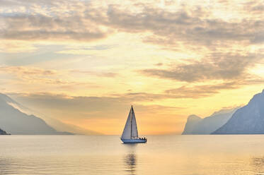 Italien, Trentino, Nago-Torbole, Segelboot segeln in der Nähe von Küstenklippen des Gardasees bei stimmungsvoller Morgendämmerung - MRF02318