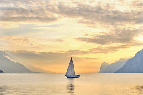 Italy, Trentino, Nago-Torbole, Sailboat sailing near coastal cliffs of Lake Garda at moody dawn - MRF02318