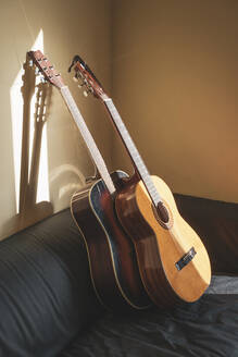 Zwei Akustikgitarren lehnen an einer Couch im Sonnenlicht - AFVF04406
