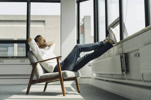 Älterer Geschäftsmann entspannt sich am Fenster in einem leeren Büro - KNSF06879