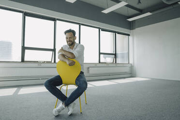 Porträt eines selbstbewussten reifen Geschäftsmannes, der auf einem gelben Stuhl in einem leeren Büro sitzt - KNSF06883
