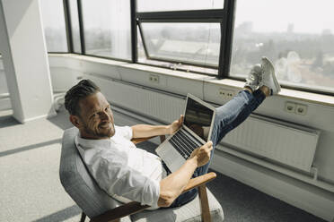 Porträt eines lächelnden reifen Geschäftsmannes mit Laptop in einem leeren Büro - KNSF06890