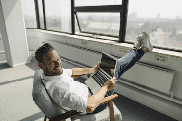 Portrait of smiling mature businessman using laptop in empty office - KNSF06890