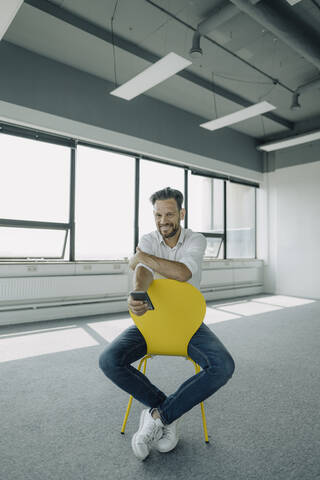 Porträt eines selbstbewussten reifen Geschäftsmannes, der auf einem gelben Stuhl in einem leeren Büro sitzt, lizenzfreies Stockfoto