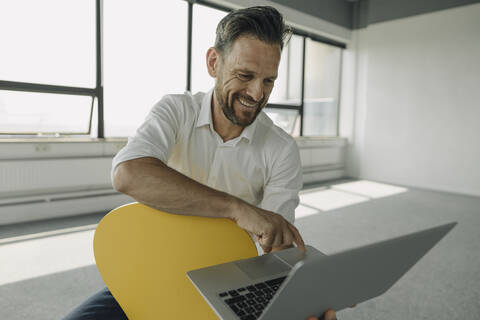 Lächelnder reifer Geschäftsmann mit Laptop in leerem Büro, lizenzfreies Stockfoto