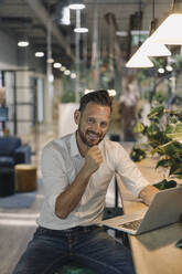 Porträt eines lächelnden reifen Geschäftsmannes, der einen Laptop in einer modernen Bürolounge benutzt - KNSF06899