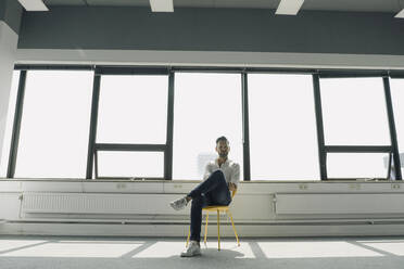 Mature businessman sitting on yellow chair in empty office - KNSF06916