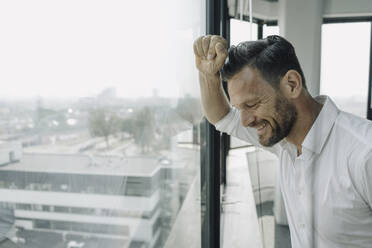 Reifer Geschäftsmann schaut im Büro aus dem Fenster - KNSF06920