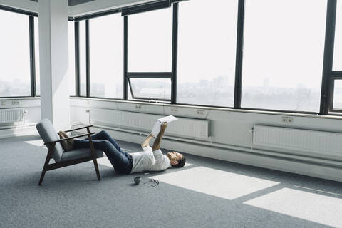 Reifer Geschäftsmann auf dem Boden liegend in leerem Büro mit Laptop, lizenzfreies Stockfoto