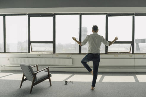Mature businessman practicing yoga in empty office - KNSF06929