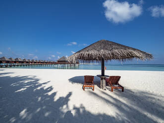 Maldives, Empty deck chairs under straw umbrella on sandy coastal beach in summer - AMF07587