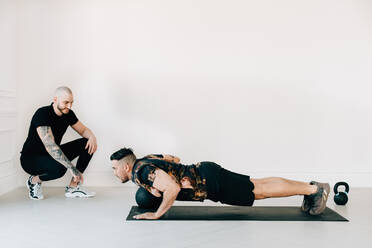 Fitness instructor observing man doing plank with medicine ball in studio - ISF23182