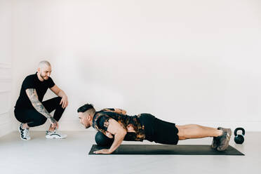 Fitness-Trainer beobachtet Mann, der im Studio eine Planke mit Medizinball macht - ISF23182