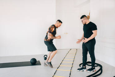 Fitness-Trainer beobachtet Mann bei der Benutzung der Agility-Leiter im Studio - ISF23186