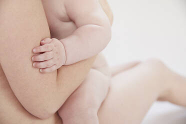 Nackte Mutter tröstet nacktes Baby auf dem Schoß liegend - ISF23219