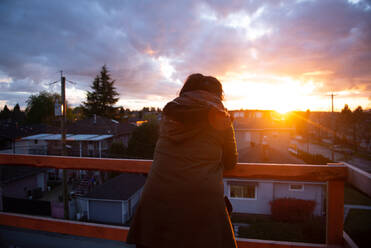 Mittlere erwachsene Frau, die vom Balkon aus den Sonnenuntergang betrachtet, Rückansicht, Vancouver, British Columbia, Kanada - ISF23236